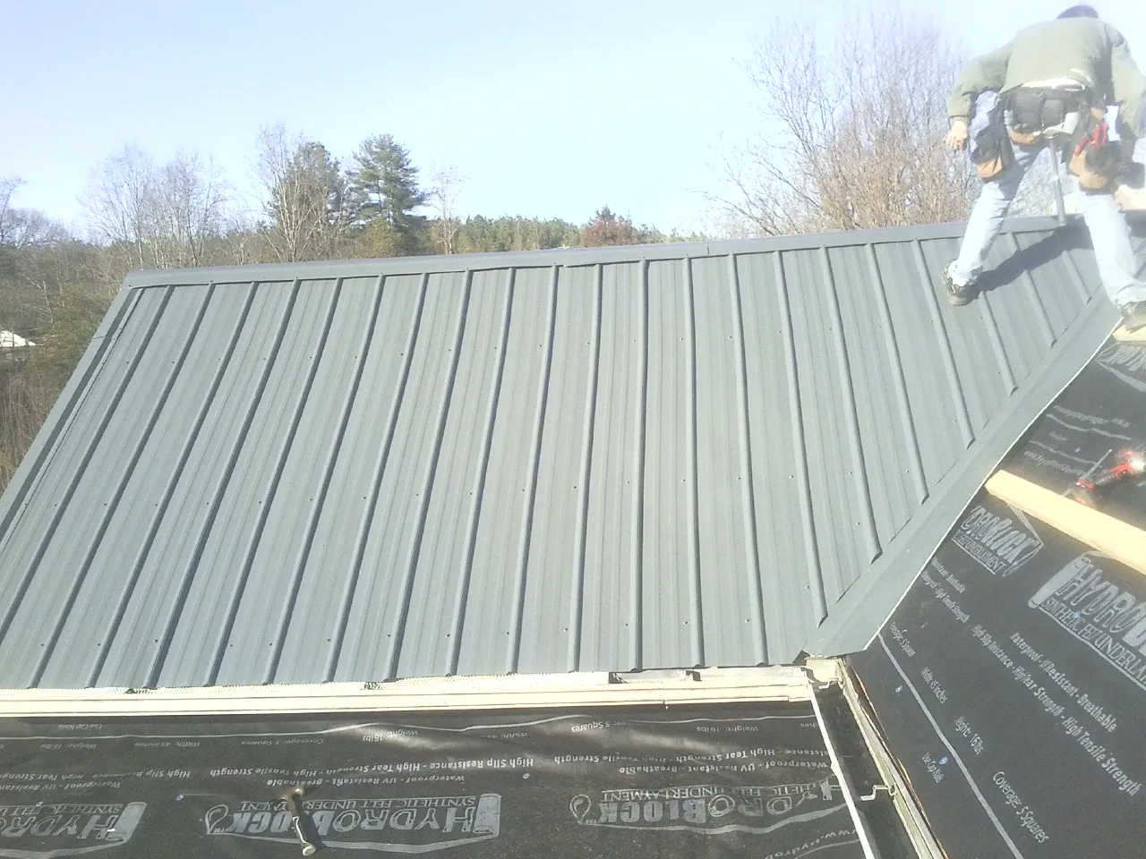Crew installing dark green standing seam panels over synthetic underlayment in Dundee